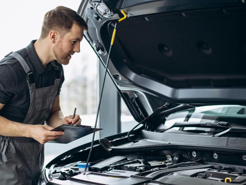 Inspector ITP verifica o masina inspectand componentele de sub capota, in cadrul unei statii ITP
